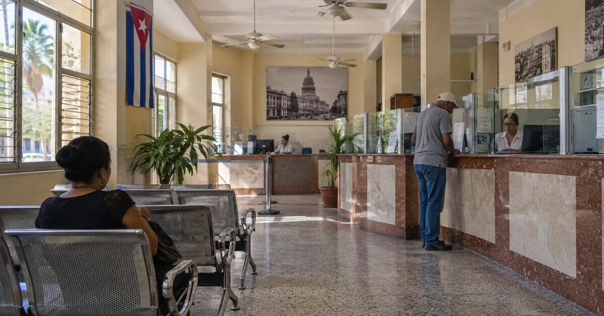 Interior de una sucursal bancaria en Cuba con clientes esperando y realizando trámites.