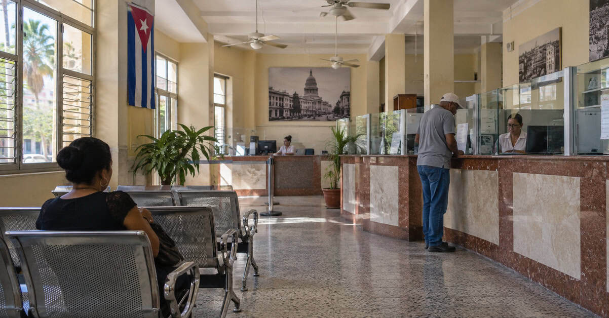 Interior de una sucursal bancaria en Cuba con clientes esperando y realizando trámites.