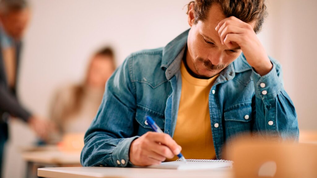 Hombre joven sentado en un aula escribiendo en una libreta