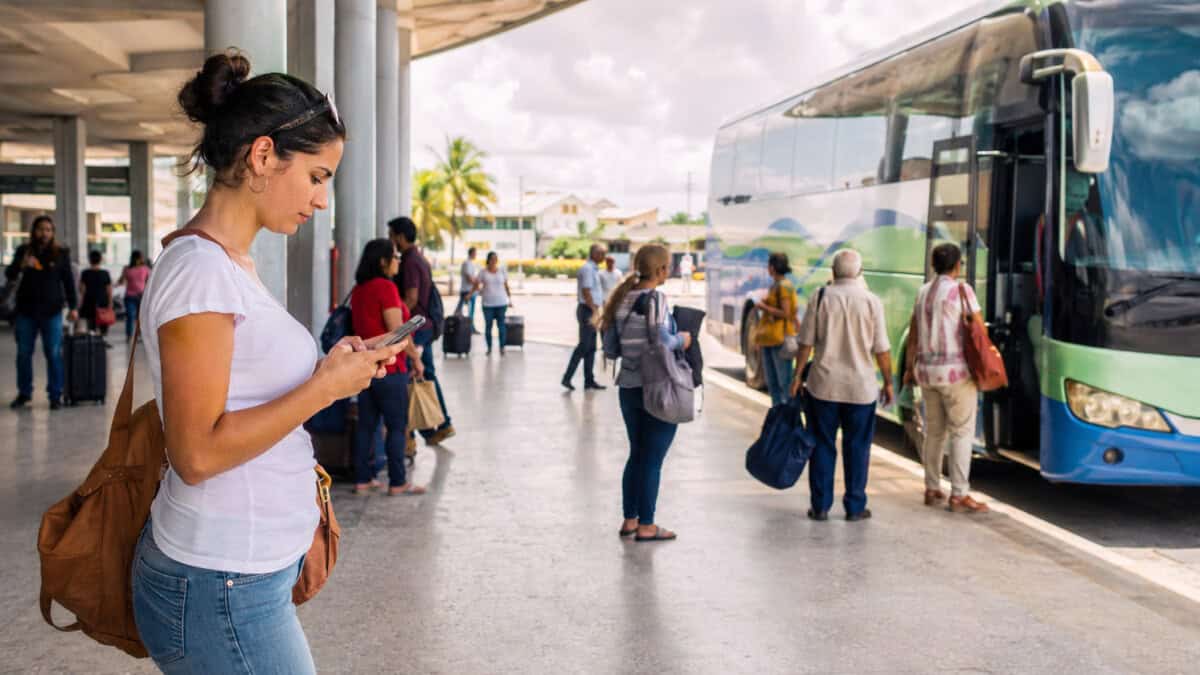 Ómnibus interprovincial en Cuba mientras una persona realiza una reserva desde el extranjero mediante una plataforma digital.