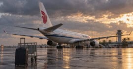 Recreación de un avión de Air China en una plataforma aeroportuaria tropical, con una maleta y un carrito en primer plano.