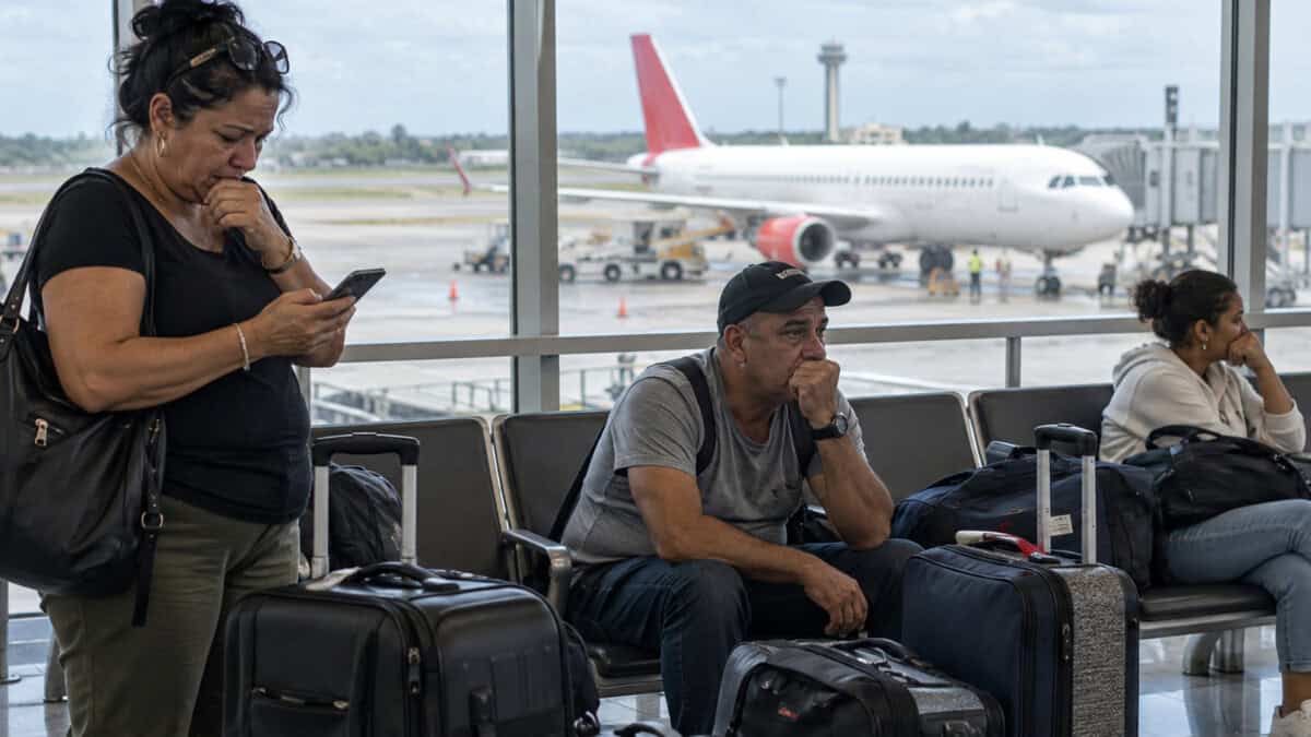 Viajeros esperan junto a sus maletas en una terminal aeroportuaria, con un avión al fondo.