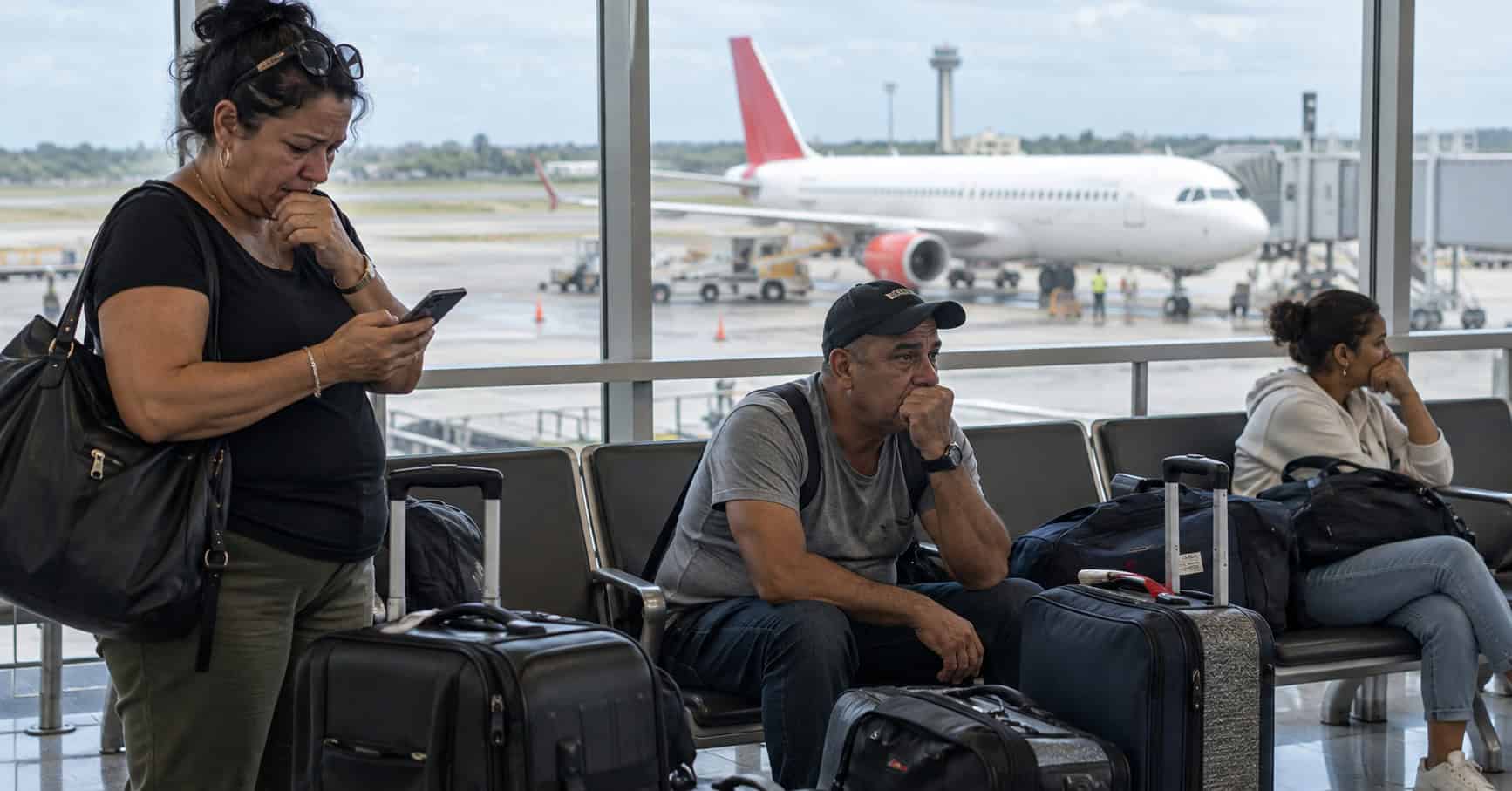 Viajeros esperan junto a sus maletas en una terminal aeroportuaria, con un avión al fondo.
