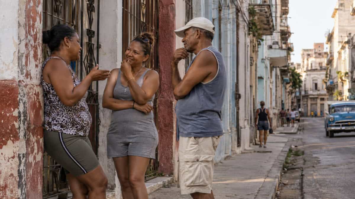 Tres adultos conversan en una calle residencial de La Habana.