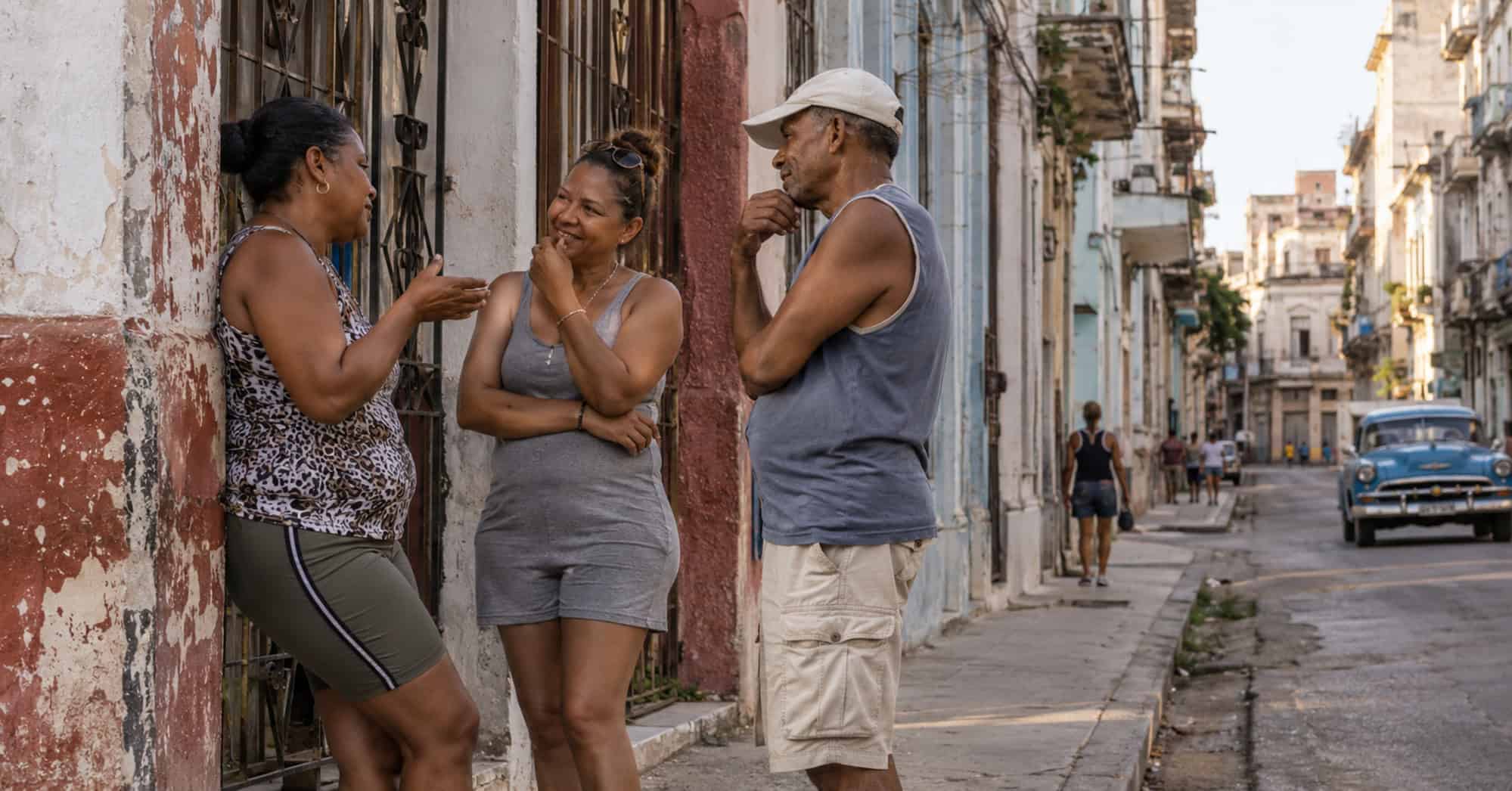Tres adultos conversan en una calle residencial de La Habana.