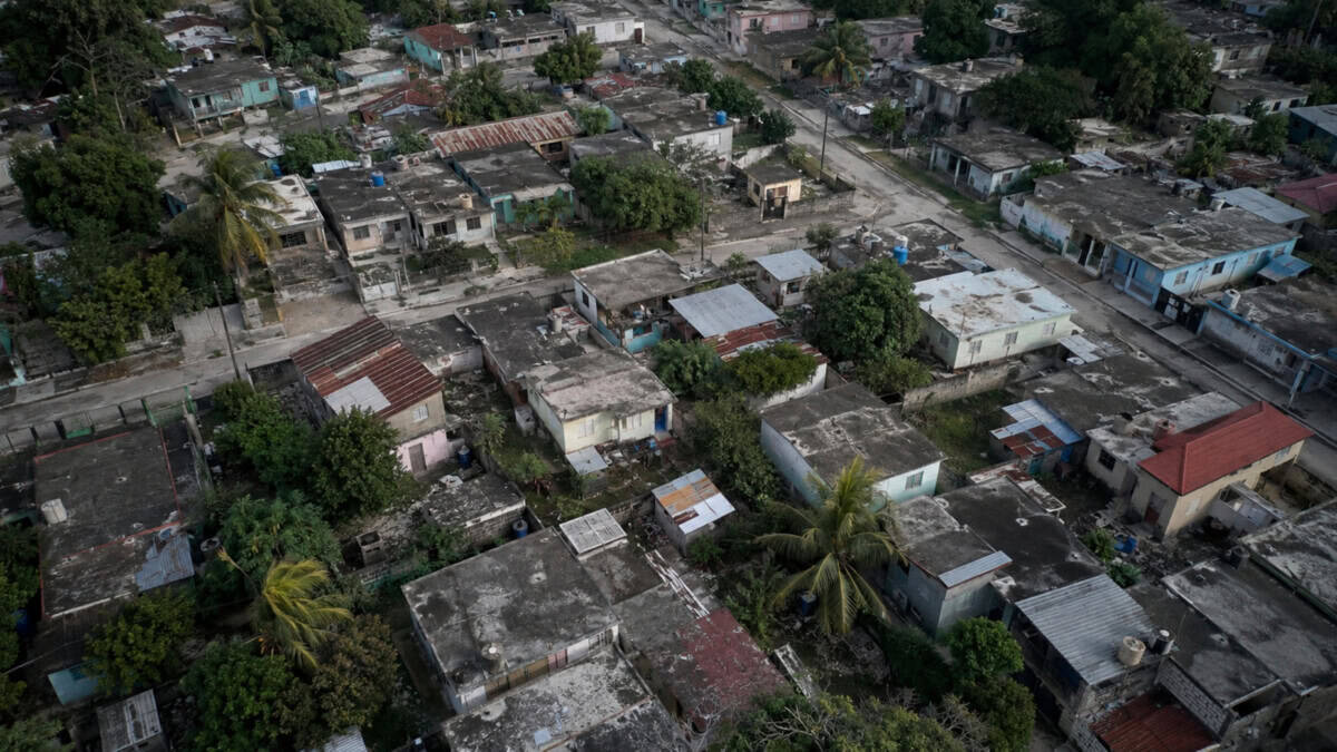 Vista aérea ilustrativa de un barrio cubano con viviendas modestas, techos desgastados y vegetación tropical.