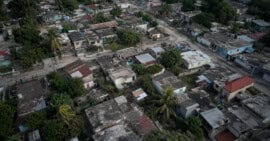 Vista aérea ilustrativa de un barrio cubano con viviendas modestas, techos desgastados y vegetación tropical.