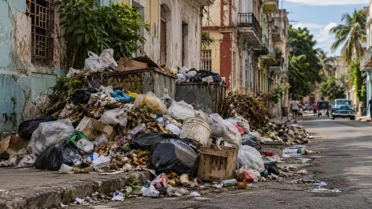 Bolsas, cartones y residuos sólidos acumulados junto a una calle deteriorada en una zona urbana de Cuba.