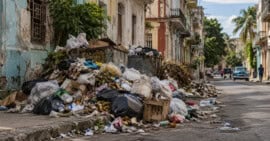 Bolsas, cartones y residuos sólidos acumulados junto a una calle deteriorada en una zona urbana de Cuba.