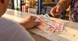 Una persona coloca billetes de pesos cubanos sobre el mostrador de un comercio.