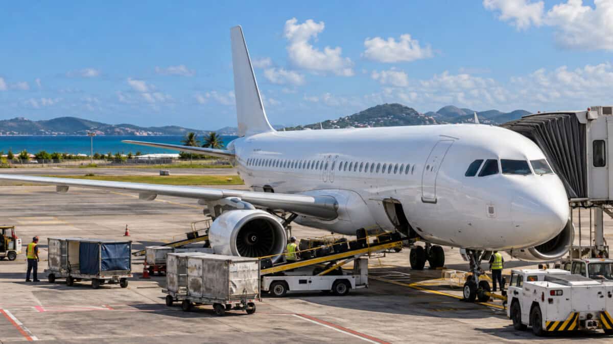 Avión comercial estacionado en la plataforma de un aeropuerto caribeño mientras el personal realiza tareas de servicio.