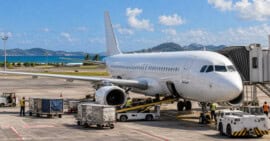 Avión comercial estacionado en la plataforma de un aeropuerto caribeño mientras el personal realiza tareas de servicio.