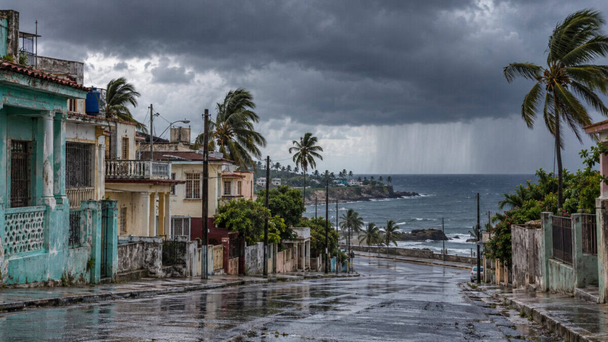 Calle húmeda y viviendas de una localidad costera cubana bajo nubes oscuras, con una cortina de lluvia sobre el mar.