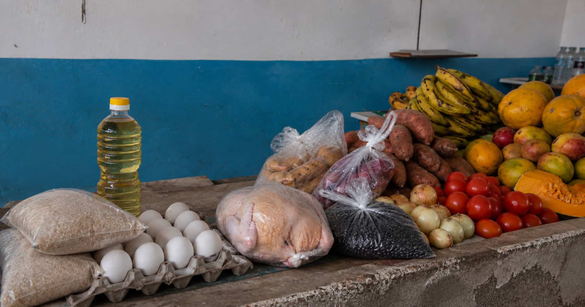 Mostrador de un mercado cubano con arroz, huevos, aceite, pollo, frijoles, viandas, tomates, cebollas y frutas.