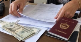 Manos organizando formularios junto a un pasaporte cubano y billetes de dólares estadounidenses.