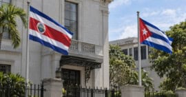 Banderas de Costa Rica y Cuba ondean en astas separadas frente a un edificio institucional.