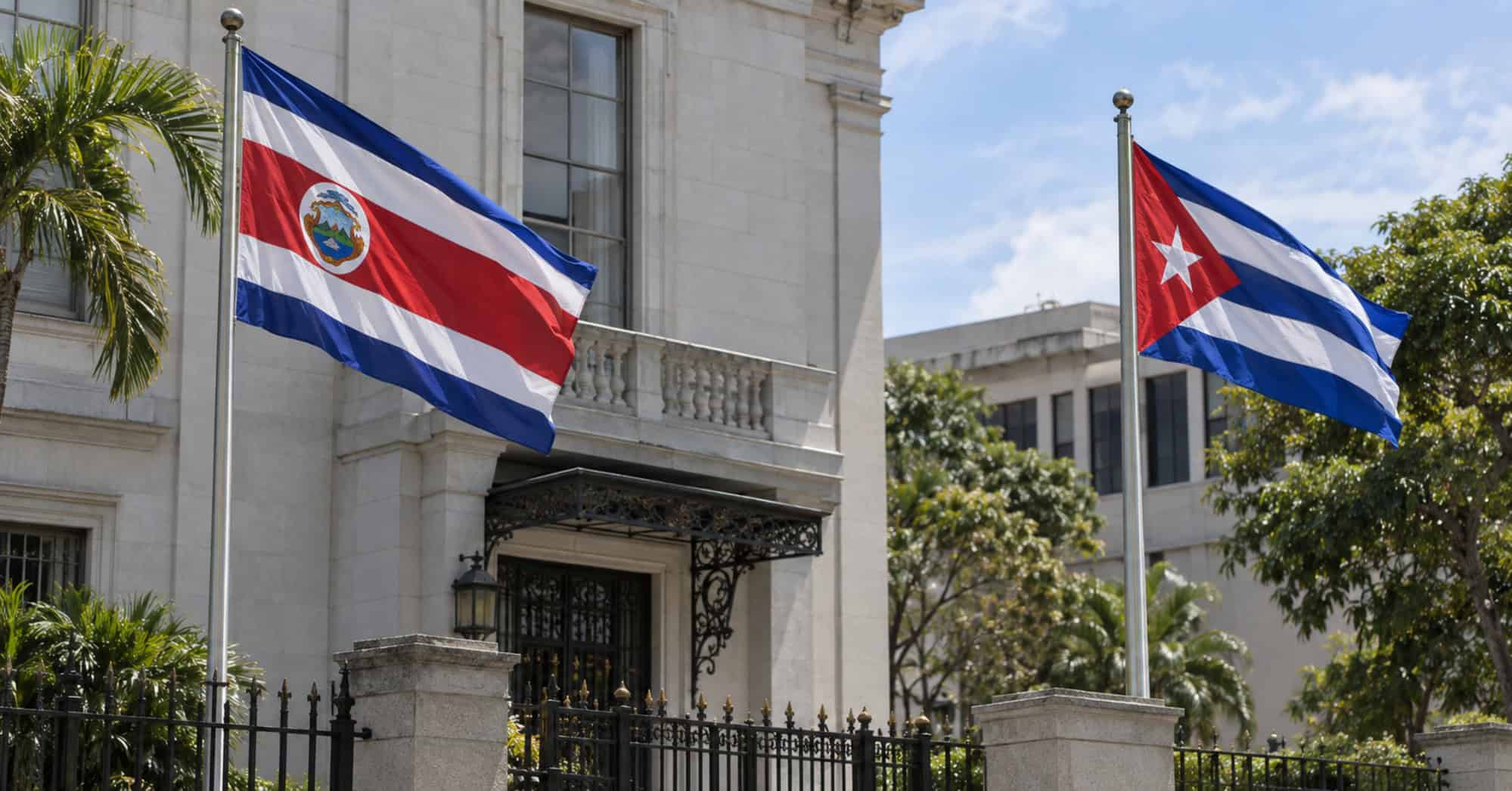 Banderas de Costa Rica y Cuba ondean en astas separadas frente a un edificio institucional.