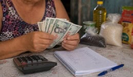 Persona contando billetes cubanos de 500 pesos con calculadora y libreta de gastos del hogar sobre una mesa.