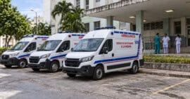 Tres ambulancias blancas con franjas rojas y azules frente a un hospital, en una imagen conceptual del sistema sanitario cubano.