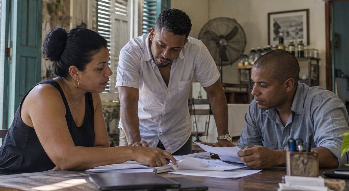 Tres emprendedores cubanos conversan y revisan documentos de trabajo dentro de un pequeño negocio privado en Cuba.