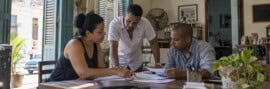 Tres emprendedores cubanos conversan y revisan documentos de trabajo dentro de un pequeño negocio privado en Cuba.