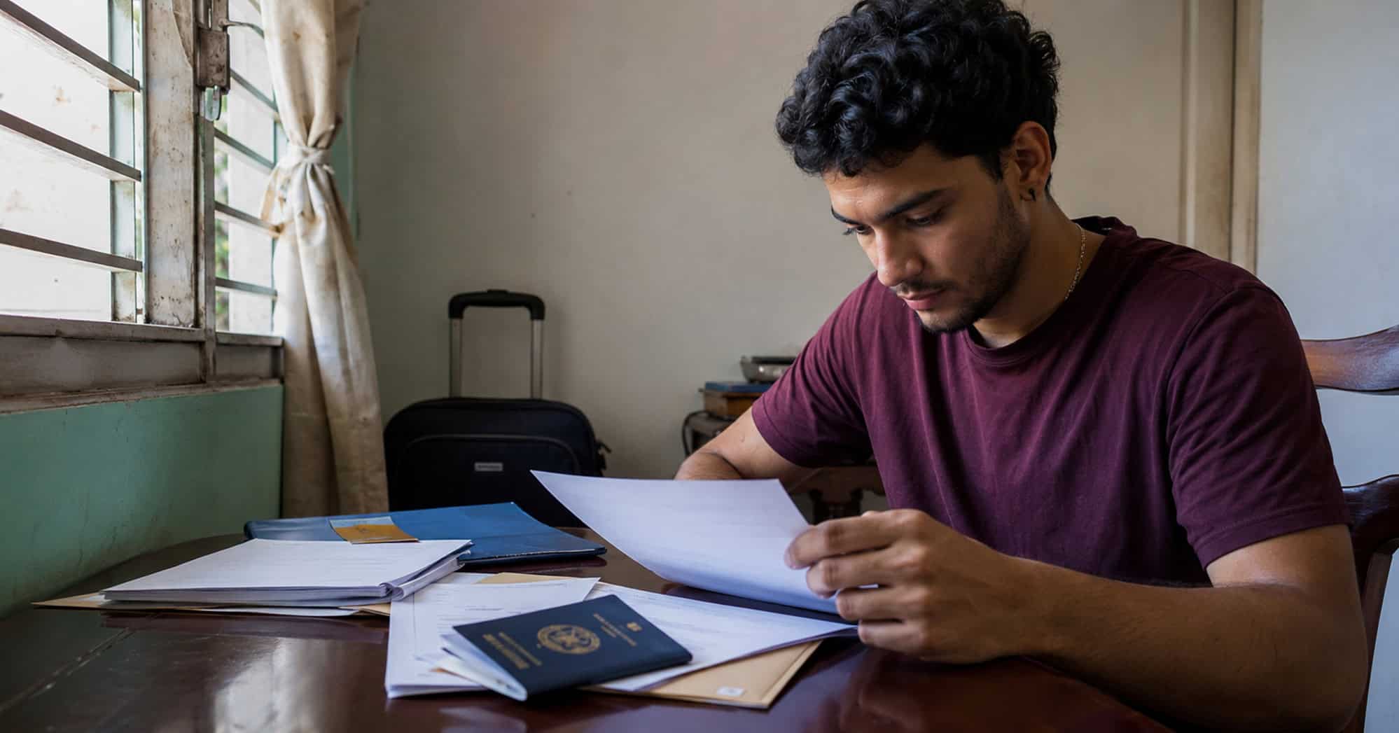 Joven adulto cubano revisa documentos académicos y su pasaporte para solicitar estudios en el extranjero.