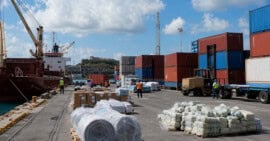 Terminal portuaria relacionada con Cuba, con contenedores, mercancías organizadas y trabajadores realizando operaciones logísticas.