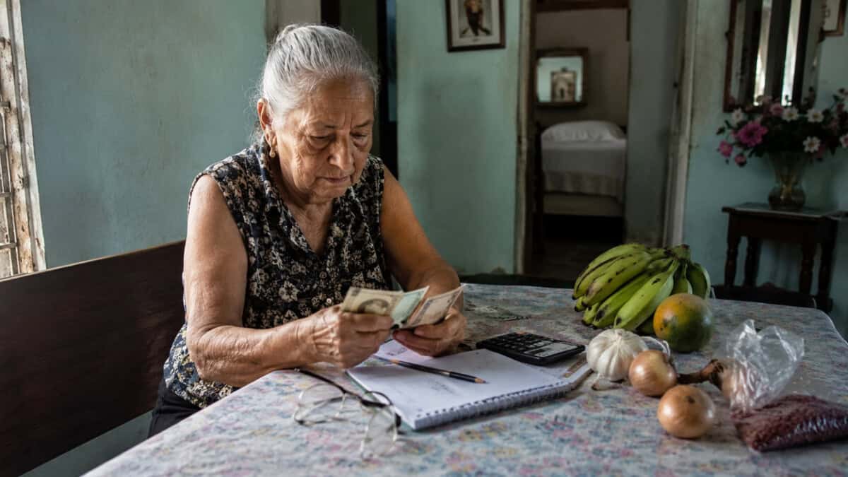 Adulta mayor cubana revisa billetes y gastos domésticos en una vivienda modesta.