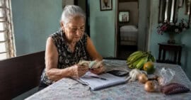 Adulta mayor cubana revisa billetes y gastos domésticos en una vivienda modesta.