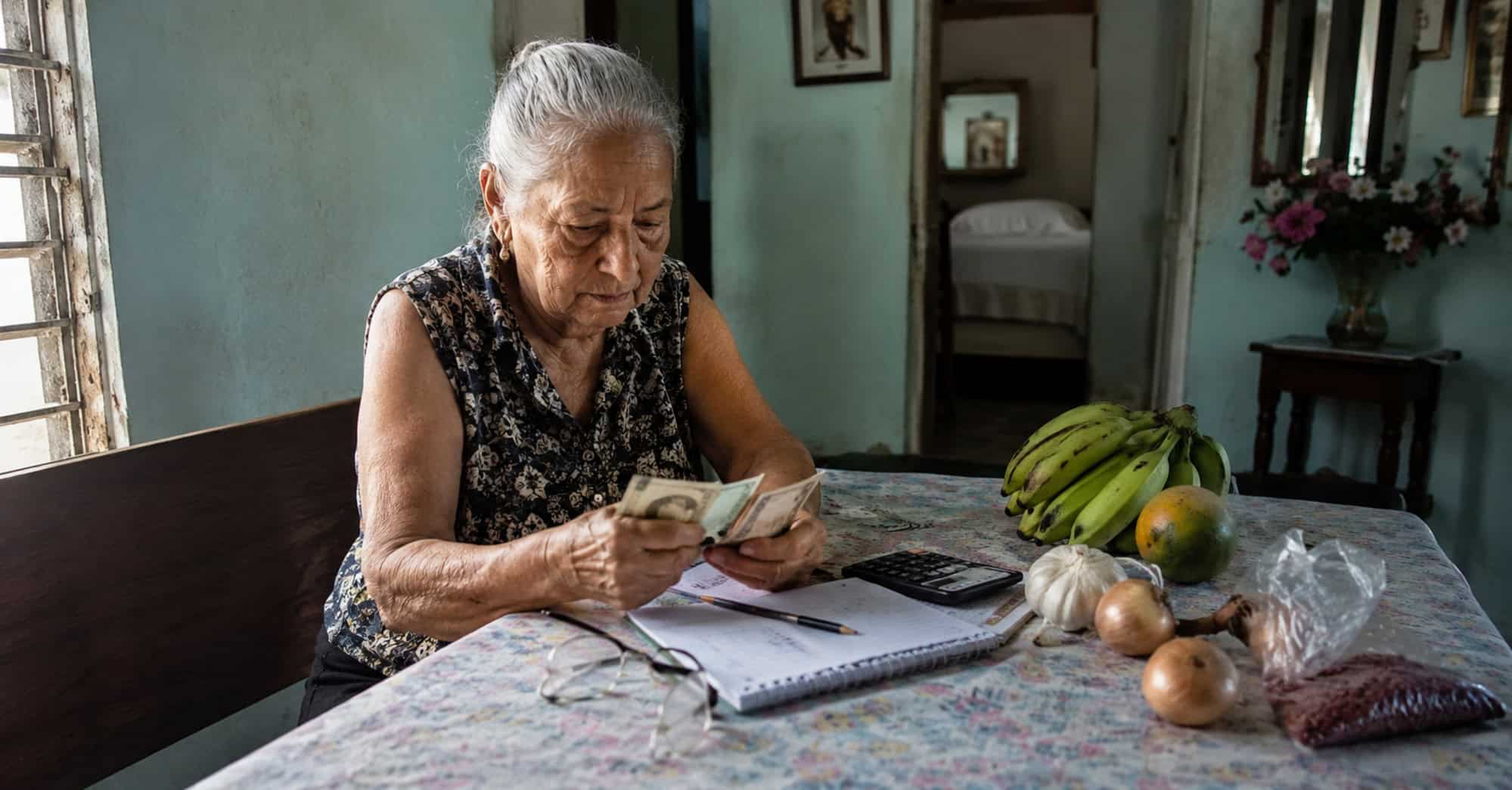 Adulta mayor cubana revisa billetes y gastos domésticos en una vivienda modesta.