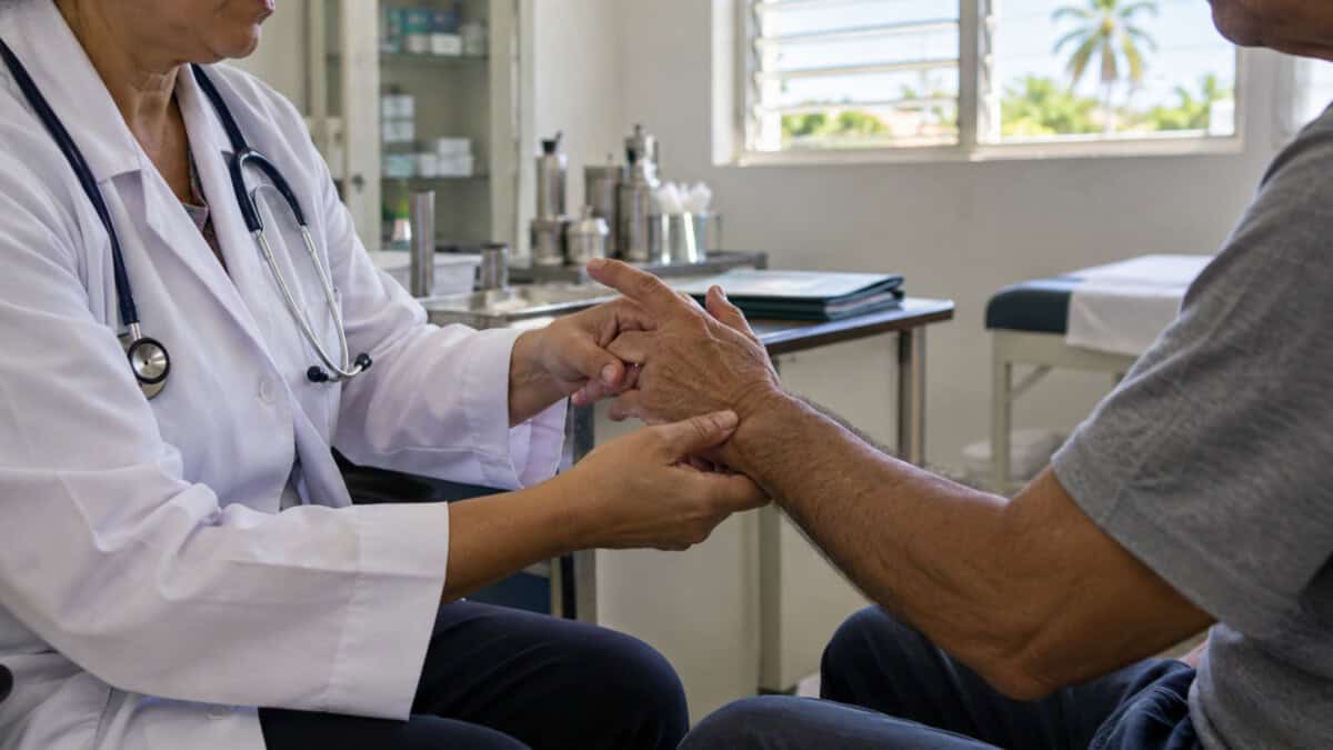 Profesional sanitario examina la mano y la muñeca de un paciente en una consulta clínica.
