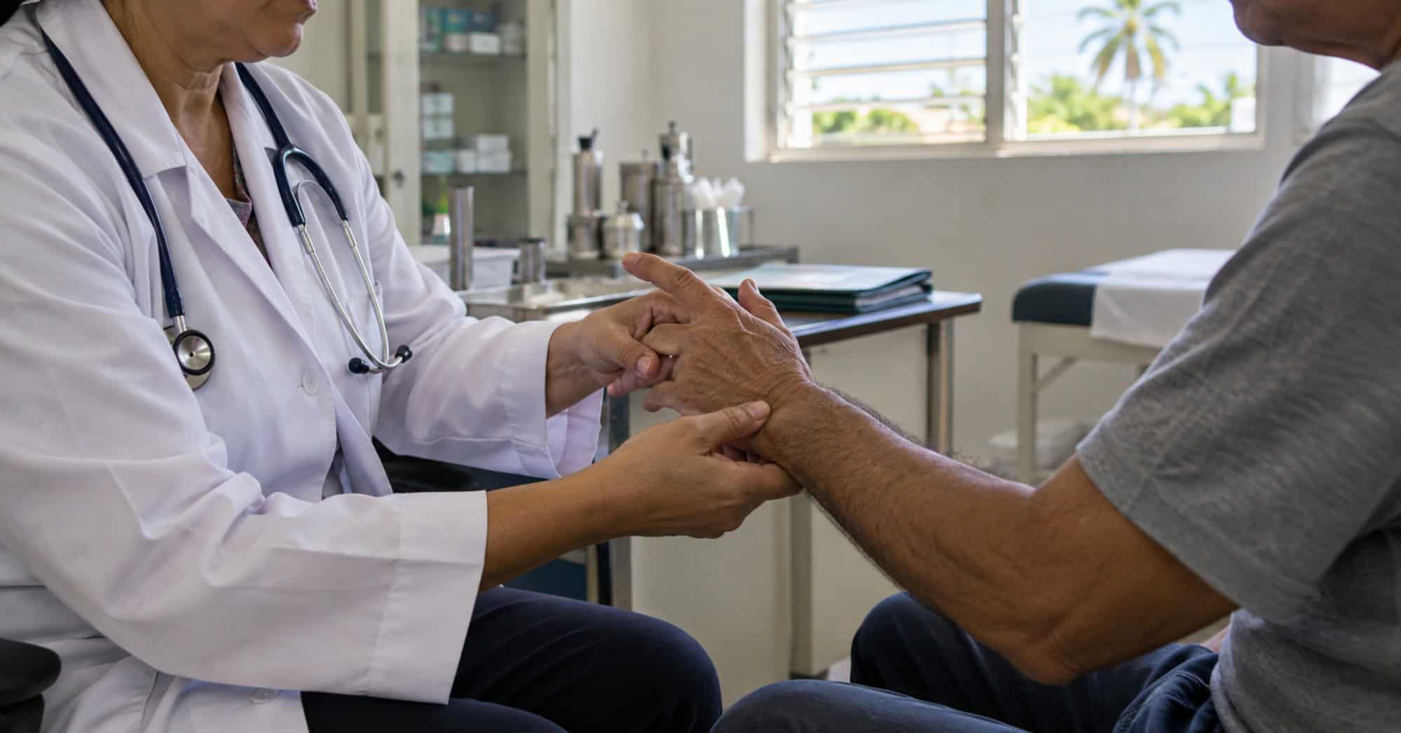 Profesional sanitario examina la mano y la muñeca de un paciente en una consulta clínica.