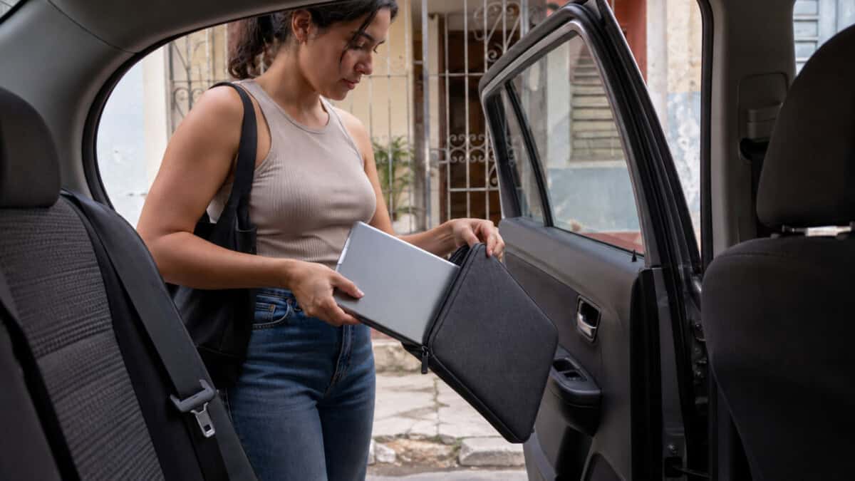 Mujer extrae una laptop de su estuche junto a la puerta abierta de un automóvil frente a una vivienda en La Habana.