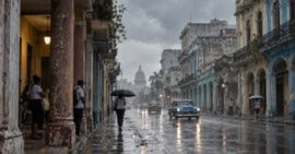 Personas se resguardan de la lluvia en una calle cubana con el pavimento mojado.