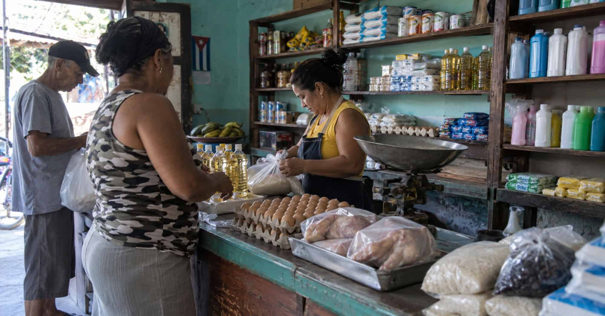Clientes compran alimentos y productos de aseo en un pequeño mercado de barrio en Cuba.