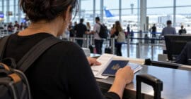 Persona de espaldas revisa un pasaporte cubano y documentos de viaje en un mostrador de aeropuerto.