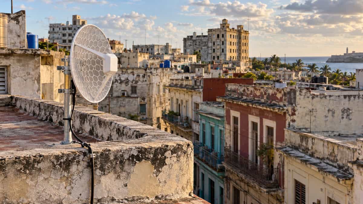 Antena inalámbrica tipo MikroTik instalada en una azotea, con edificios residenciales cubanos al fondo.