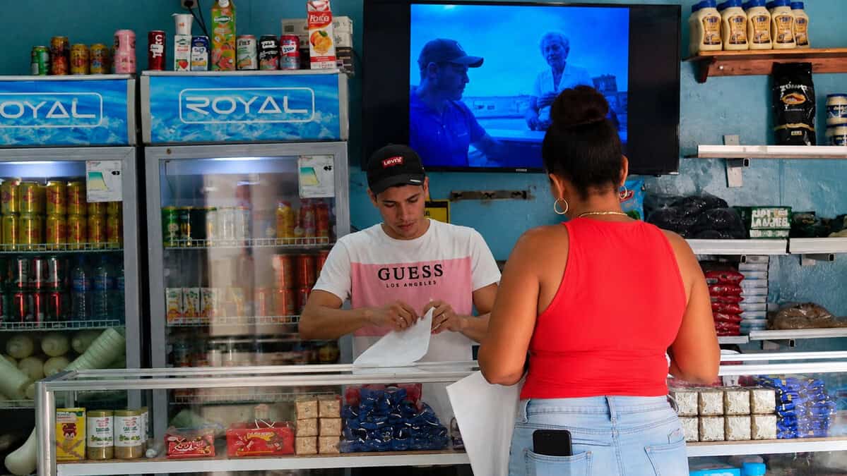 Cliente realizando una compra en una mipyme cubana con productos en exhibición y dependiente atendiendo detrás del mostrador.