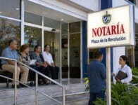 Exterior de la Notaría Plaza de la Revolución en Cuba con ciudadanos esperando atención y cartel identificativo del edificio.