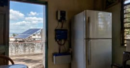 Refrigerador doméstico conectado a un sistema de energía solar con batería, inversor y paneles solares en una vivienda cubana.