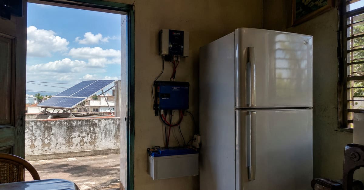 Refrigerador doméstico conectado a un sistema de energía solar con batería, inversor y paneles solares en una vivienda cubana.