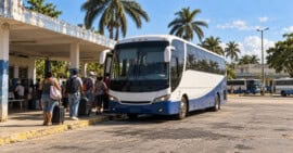 Ómnibus moderno estacionado en un parqueo de transporte interprovincial en Cuba, con viajeros y equipajes.