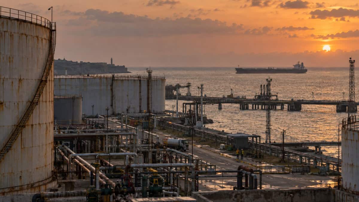 Terminal portuaria de combustible en Cuba con tanques de almacenamiento y un buque petrolero a distancia al atardecer.