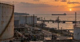 Terminal portuaria de combustible en Cuba con tanques de almacenamiento y un buque petrolero a distancia al atardecer.
