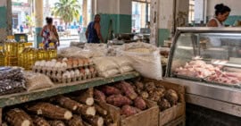 aceites, huevos, arroz y viandas en un mercado de alimentos, junto a una vitrina con pollo y carne de cerdo