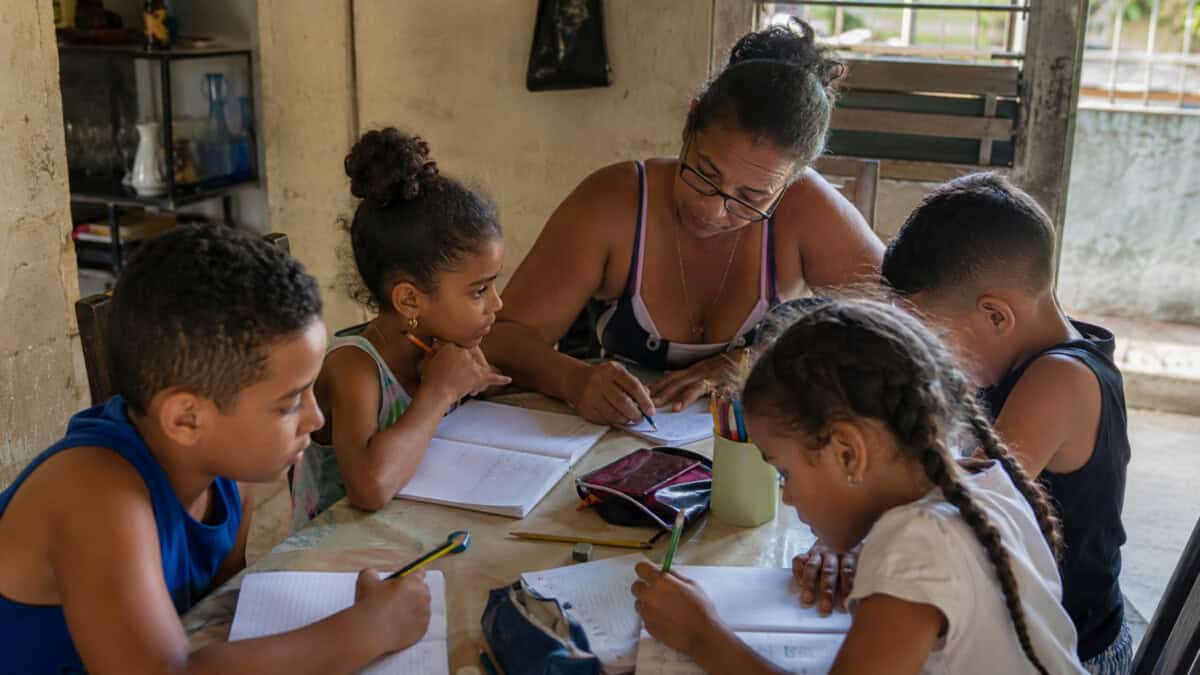 Profesora cubana impartiendo una clase particular a un pequeño grupo de niños en una vivienda sencilla