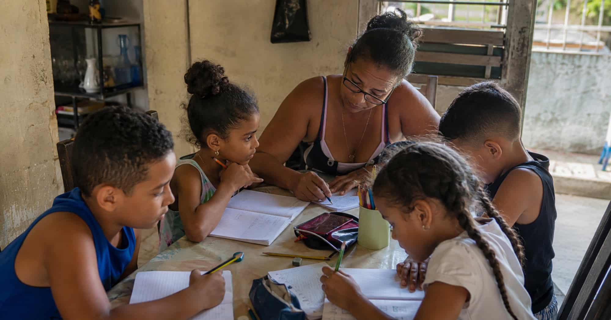 Profesora cubana impartiendo una clase particular a un pequeño grupo de niños en una vivienda sencilla