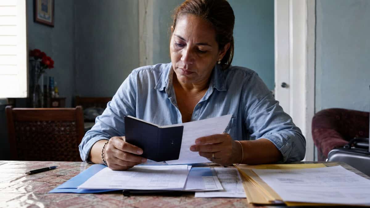 Mujer cubana revisando su pasaporte y documentos relacionados con un proceso de visa de inmigrante hacia Estados Unidos.