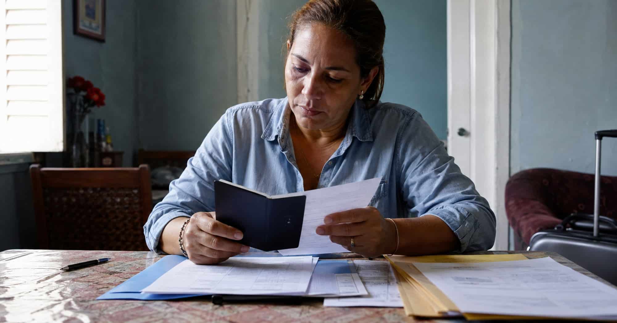 Mujer cubana revisando su pasaporte y documentos relacionados con un proceso de visa de inmigrante hacia Estados Unidos.