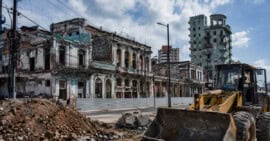 Maquinaria de construcción frente a edificios deteriorados e infraestructura urbana envejecida en Cuba, representación del proceso de reconstrucción del país.